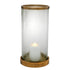 A cylindrical glass hurricane with ribbed texture and antique brass base and rim, containing a lit candle.