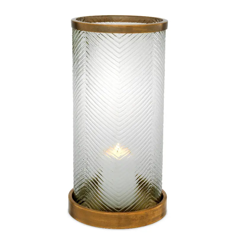 A cylindrical glass hurricane with ribbed texture and antique brass base and rim, containing a lit candle.