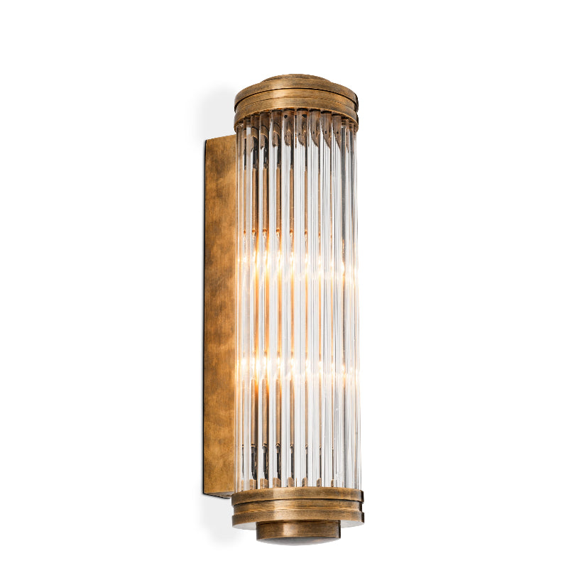 A vintage brass finished wall lamp with a ribbed and bevelled clear glass shade, featuring a geometric pattern.