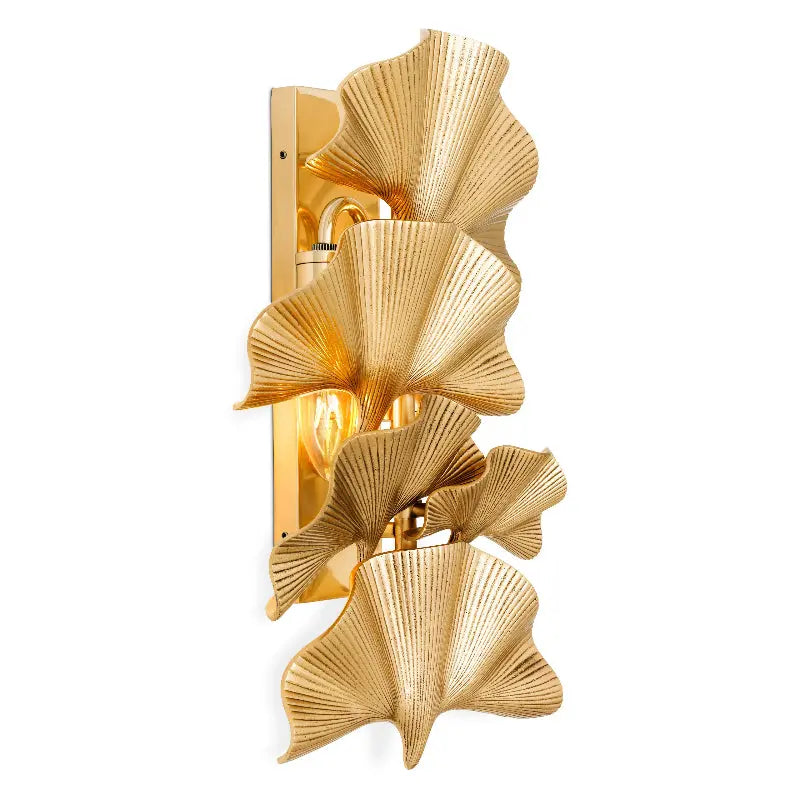 A glamorous wall sconce with five polished brass palm leaves, in an elegant curved arrangement, with lit candles on the sides.