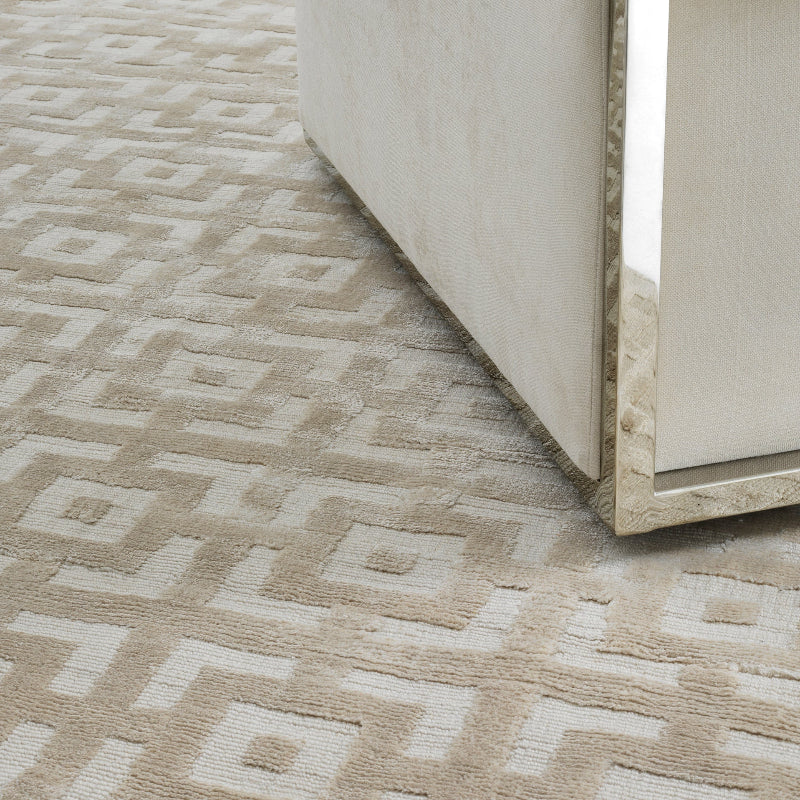 A corner of a beige woven carpet with a geometric pattern, showing a textured design.