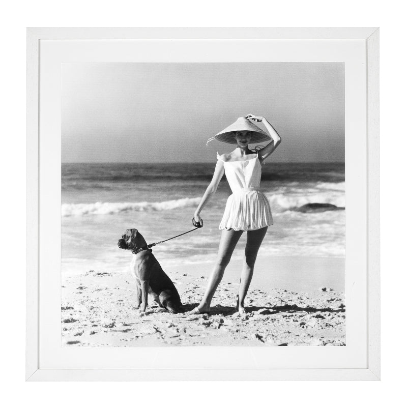 A black and white photograph of a woman in a swimsuit with a dog on a leash, taken by Laurence Le Guay for Vogue in 1956, framed in a white wooden frame with clear glass.