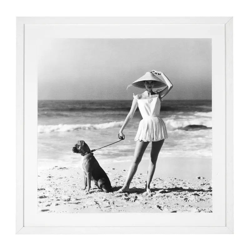 A black and white photograph of a woman in a swimsuit with a dog on a leash, taken by Laurence Le Guay for Vogue in 1956, framed in a white wooden frame with clear glass.