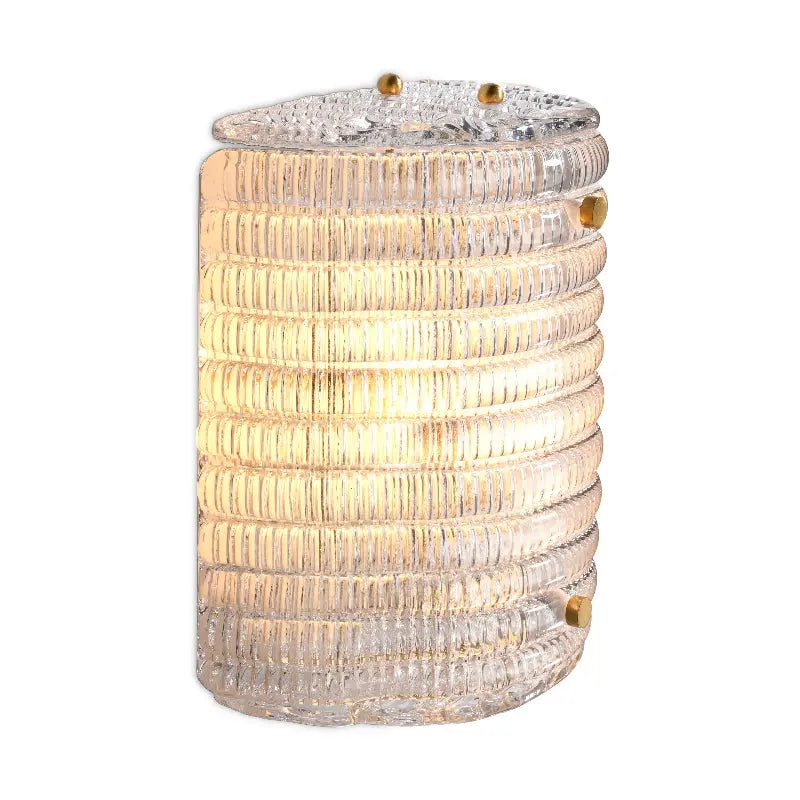 A wall-mounted lamp with a semi-circular shade of clear glass and an antique brass finish.
