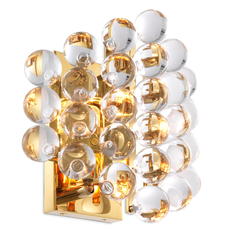 Gold-finished wall lamp with clear glass spheres, designed to provide a warm light.