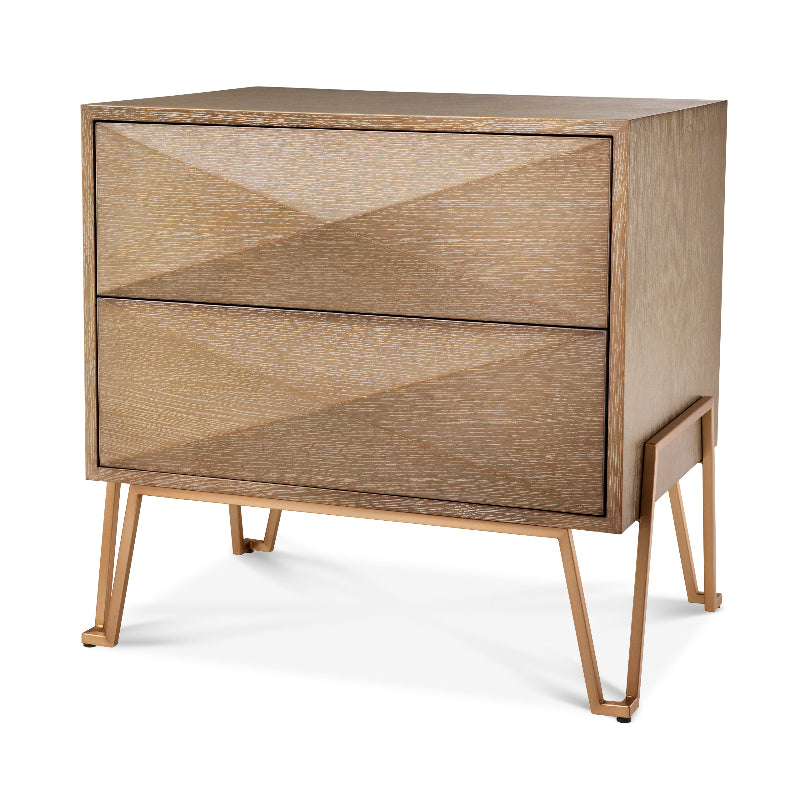 A washed oak veneer nightstand with a brushed brass finished frame, featuring triangular silhouettes on the cabinet doors and resting on splayed wooden legs.
